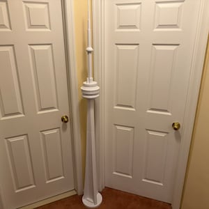 May include: A white model of the CN Tower, a famous landmark in Toronto, Canada. The model is standing in a room with white doors and beige walls.