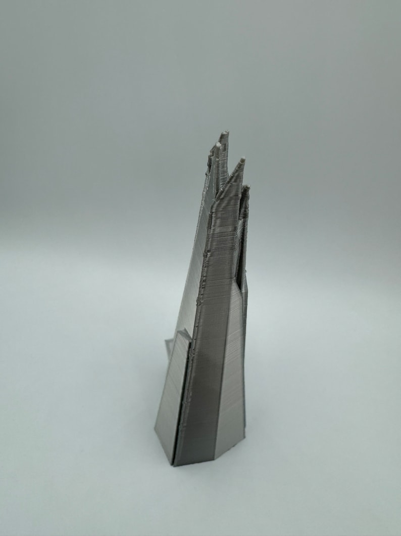 May include: A 3D printed model of a skyscraper, made of a silver-colored plastic. The model is detailed and has a sharp, angular design.