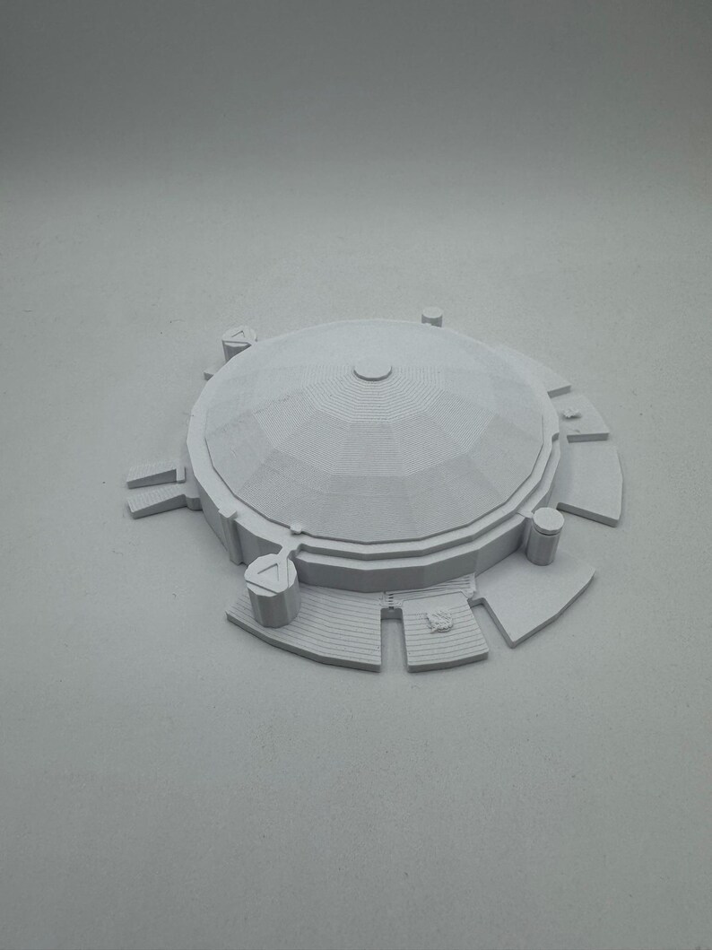 May include: A light gray, 3D-printed model of a domed structure. The model features a circular base with rectangular and triangular extensions, steps, and cylindrical pillars. The dome has a segmented, textured surface.