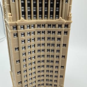 Op de afbeelding: Een gedetailleerd model van een hoog, beige gebouw met veel ramen. Het gebouw heeft een gebogen gevel en een decoratieve kroonlijst.