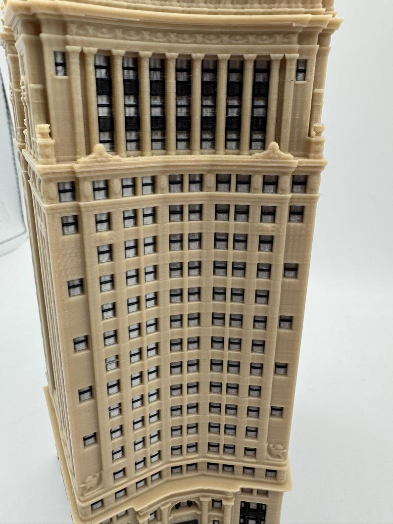 Op de afbeelding: Een gedetailleerd model van een hoog, beige gebouw met veel ramen. Het gebouw heeft een gebogen gevel en een decoratieve kroonlijst.