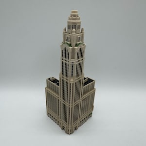 May include: A detailed model of a tall building with a tower, featuring a beige color scheme with darker accents. The building has many windows and architectural details, resembling a historic skyscraper.