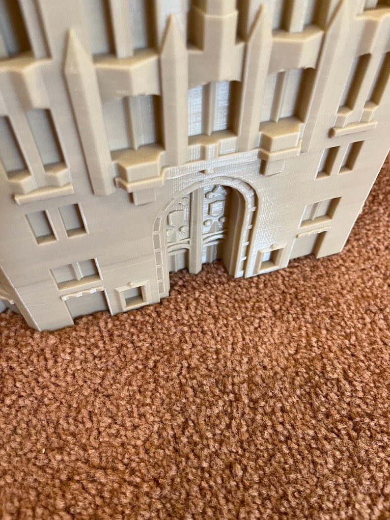 May include: A beige 3D printed model of a building with an arched doorway and multiple windows. The building has a detailed facade with decorative elements.