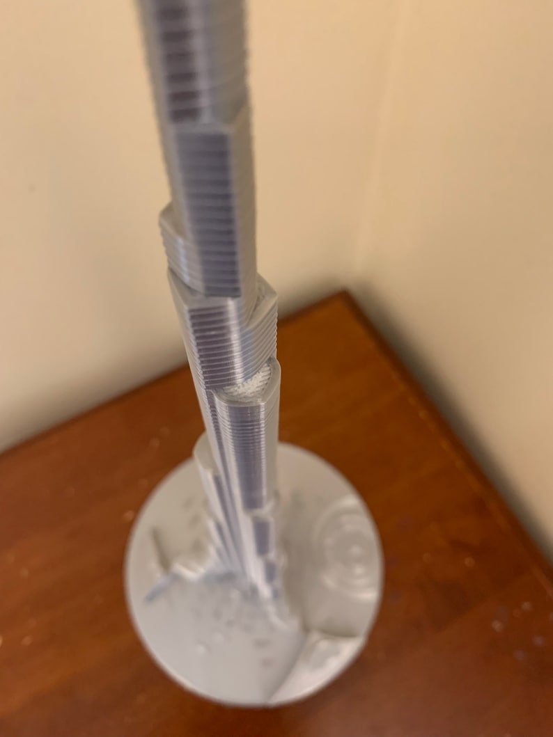 May include: A white 3D printed model of a skyscraper on a white base.