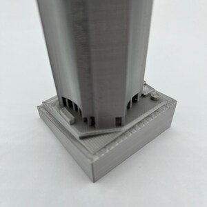 May include: A gray 3D printed model of a skyscraper with a square base.