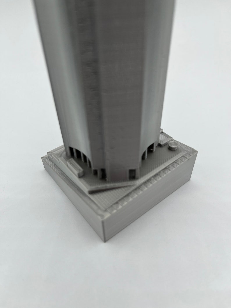 May include: A gray 3D printed model of a skyscraper with a square base.