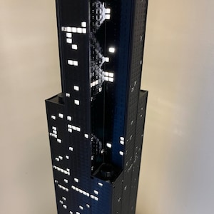 May include: A black and white model of a skyscraper with lights illuminating the windows.
