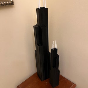 May include: Two black 3D printed models of skyscrapers with white antenna details. The models are on a wooden surface.