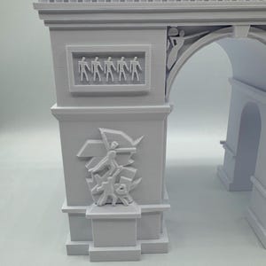 Może przedstawiać: Jasnoszara miniaturowa replika Łuku Triumfalnego. Model architektoniczny zawiera szczeg&oacute;łowe rzeźby postaci i rzeźby reliefowe. Łuk jest klasycznym pomnikiem.