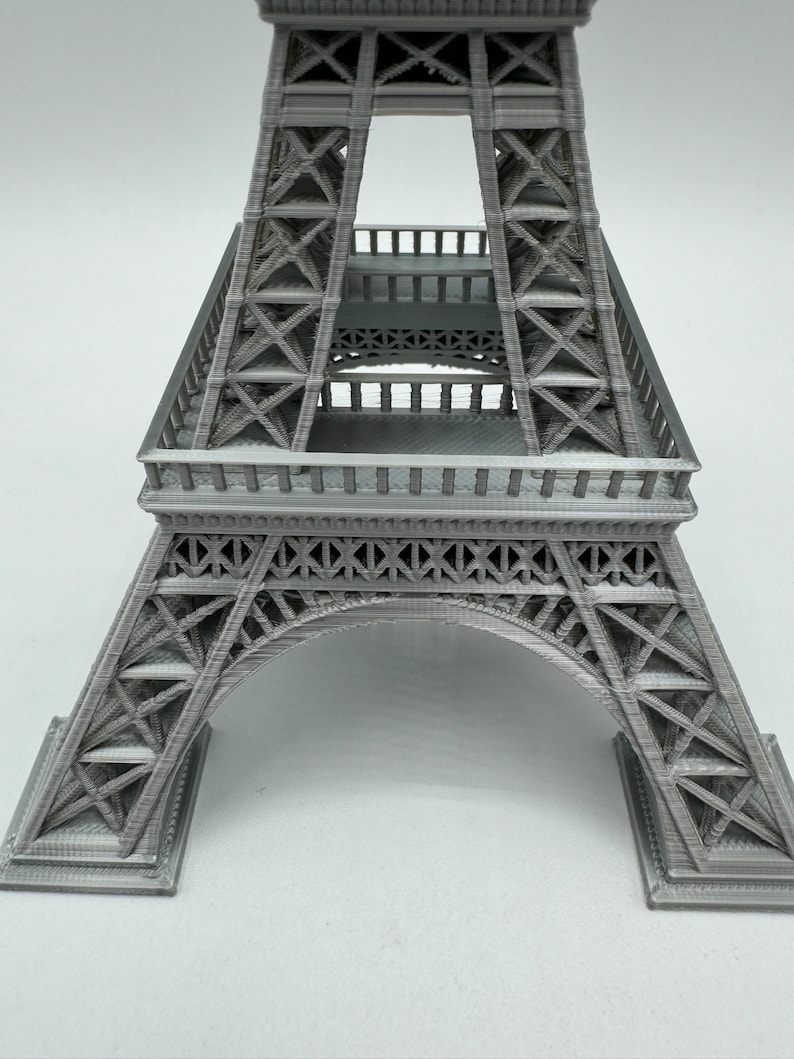 May include: A gray 3D printed model of the Eiffel Tower. The model is detailed and shows the intricate structure of the tower.