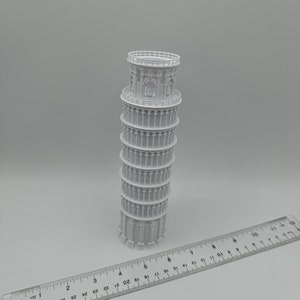 May include: A white plastic model of the Leaning Tower of Pisa, approximately 6 inches tall, with a ruler for scale.