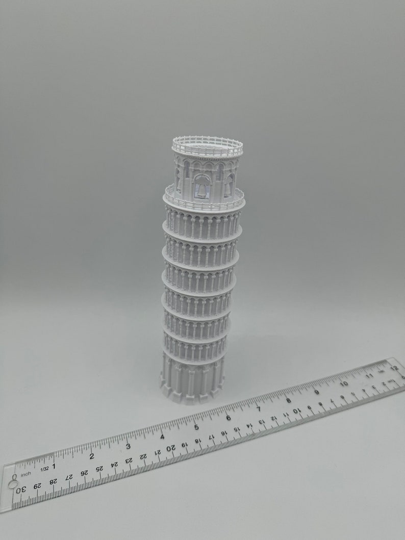 May include: A white plastic model of the Leaning Tower of Pisa, approximately 6 inches tall, with a ruler for scale.