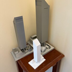 May include: Three miniature model buildings, two are gray and one is white. The buildings are on a wooden table.