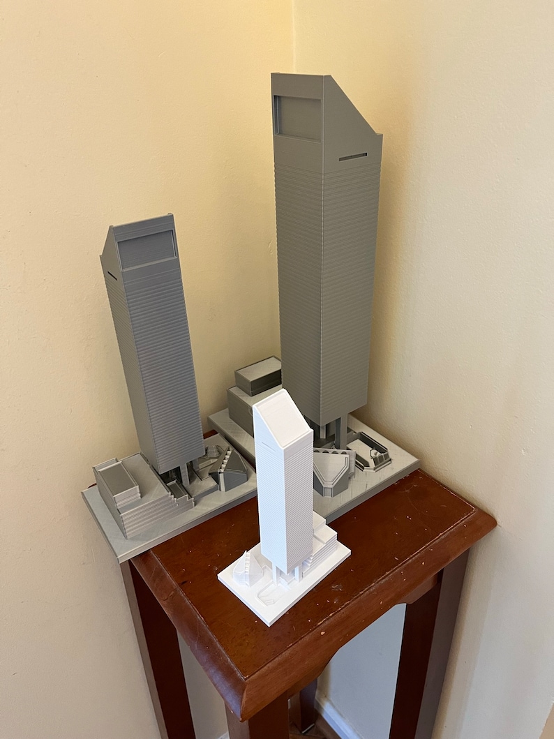 May include: Three miniature model buildings, two are gray and one is white. The buildings are on a wooden table.