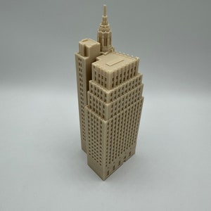 Pu&ograve; includere: Un modello di grattacielo stampato in 3D di colore beige con un tetto a punta e un edificio pi&ugrave; piccolo attaccato al lato.