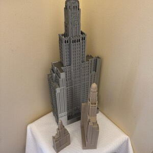 May include: Three gray 3D printed models of skyscrapers. The tallest building is approximately 12 inches tall and the two smaller buildings are approximately 4 inches tall.