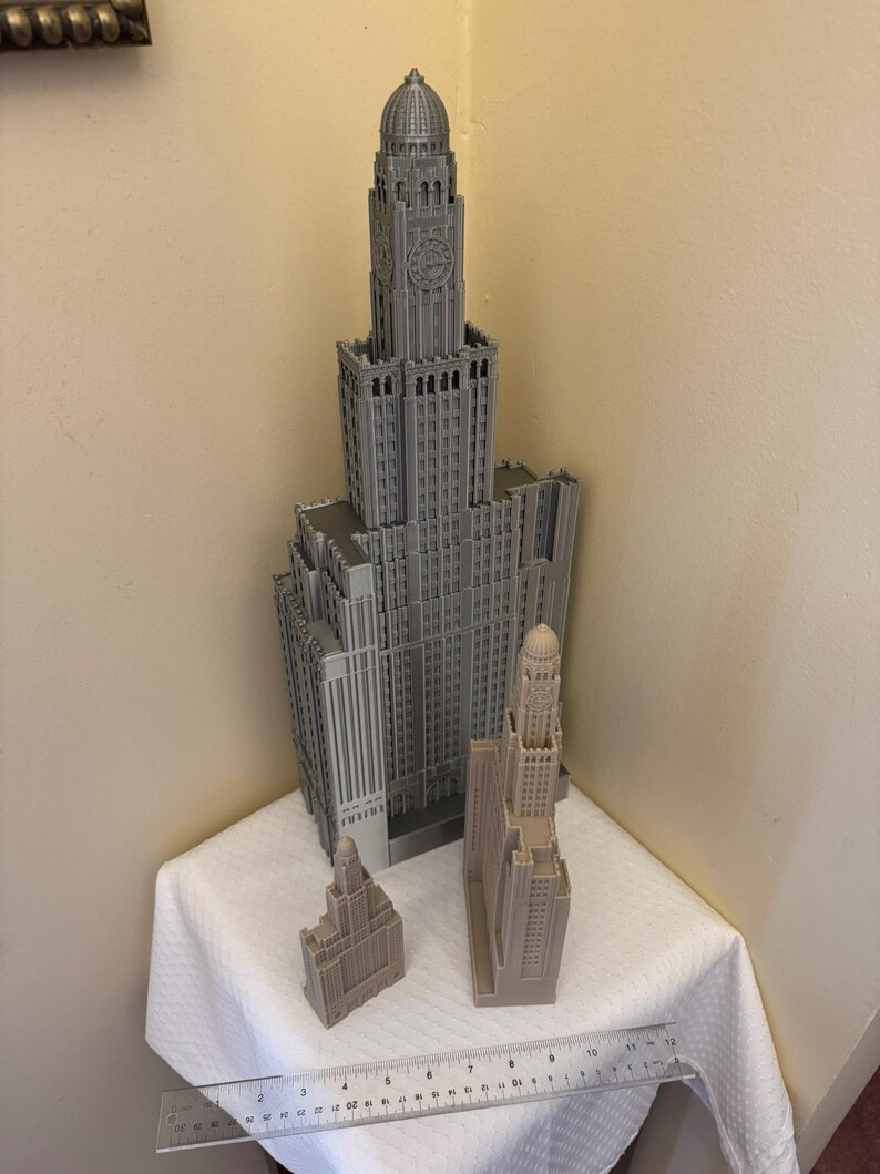 May include: Three gray 3D printed models of skyscrapers. The tallest building is approximately 12 inches tall and the two smaller buildings are approximately 4 inches tall.