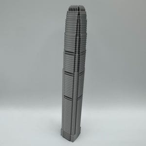 May include: A gray, miniature replica of a skyscraper. The building has a rectangular base and tapers towards the top. The facade features numerous horizontal lines and vertical divisions, with a detailed top section.
