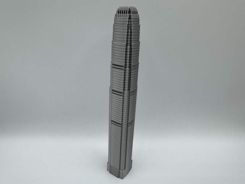 May include: A gray, miniature replica of a skyscraper. The building has a rectangular base and tapers towards the top. The facade features numerous horizontal lines and vertical divisions, with a detailed top section.