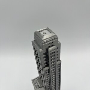 May include: A detailed model of a tall, gray skyscraper with a flat roof and many windows. The model is made of a smooth, gray material and appears to be 3D printed.