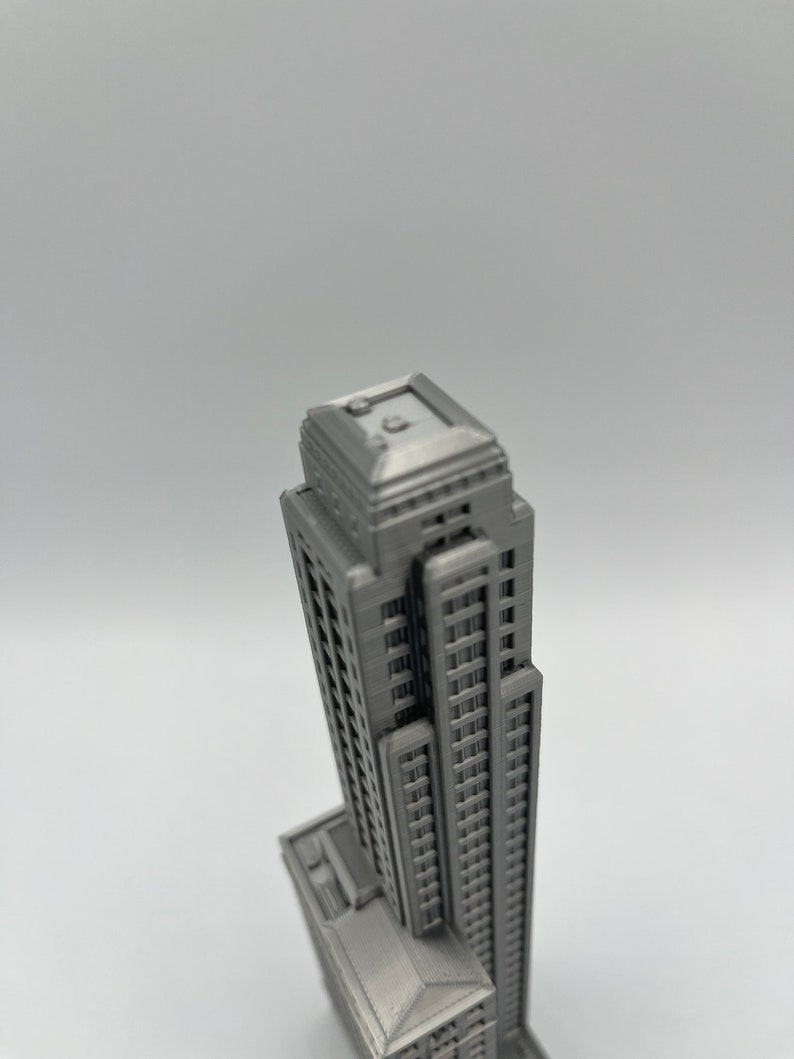 May include: A detailed model of a tall, gray skyscraper with a flat roof and many windows. The model is made of a smooth, gray material and appears to be 3D printed.