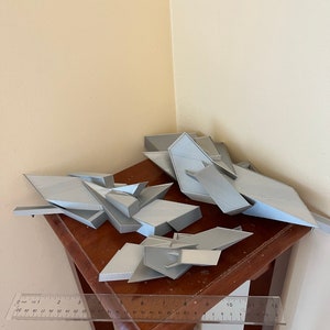 May include: Four gray 3D printed geometric shapes on a wooden table with a ruler measuring 12 inches.