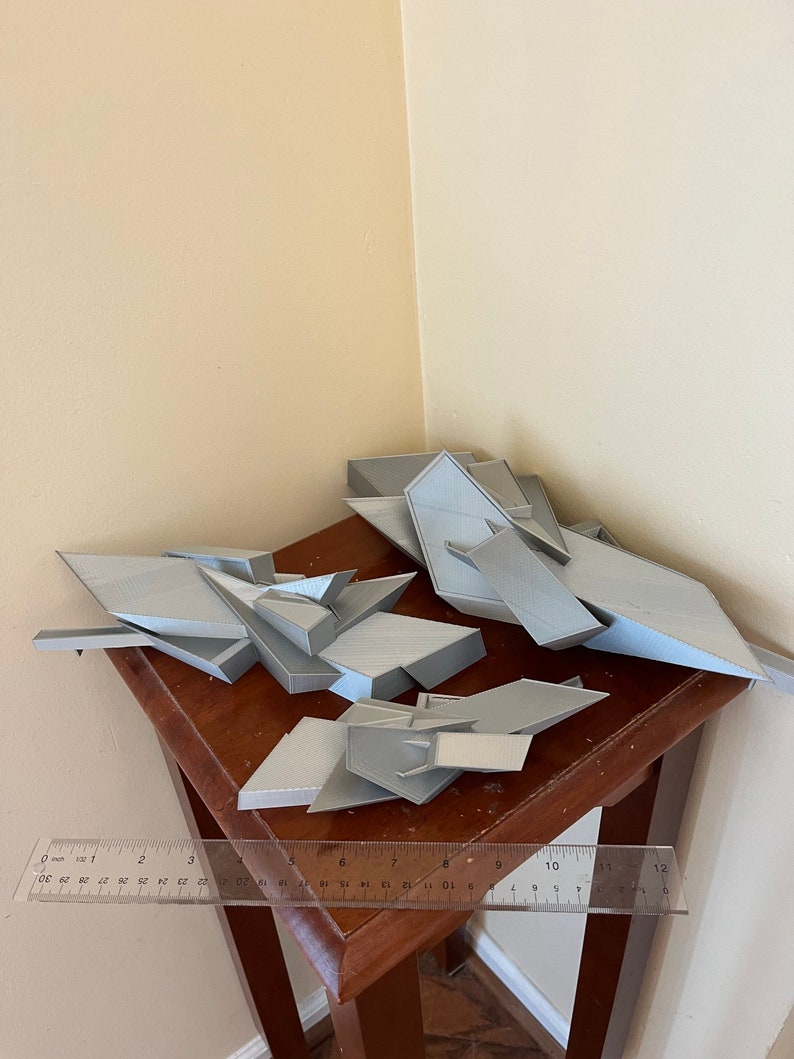 May include: Four gray 3D printed geometric shapes on a wooden table with a ruler measuring 12 inches.