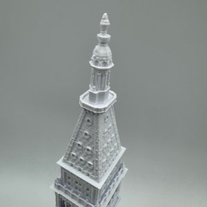 May include: A white 3D printed model of a tall building with a pointed spire and intricate details.