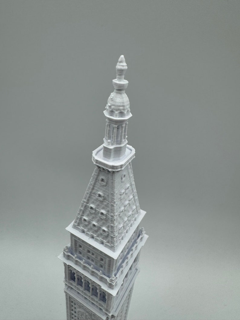 May include: A white 3D printed model of a tall building with a pointed spire and intricate details.