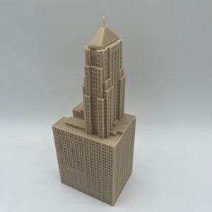 May include: A detailed miniature model of a tall, beige skyscraper with a pointed roof. The model is made of plastic and has a realistic design.