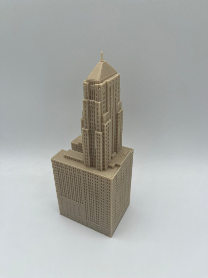 May include: A detailed miniature model of a tall, beige skyscraper with a pointed roof. The model is made of plastic and has a realistic design.