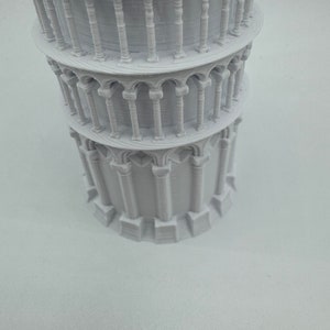 May include: A white 3D printed model of the Leaning Tower of Pisa. The model is detailed with arches and columns.