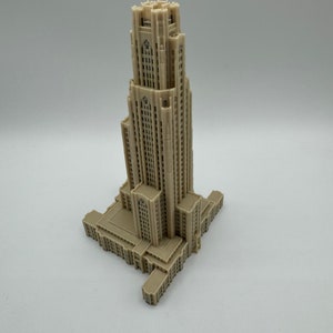 May include: A detailed 3D printed model of a tall, beige building with a pointed roof and many windows. The building has a rectangular base and is set against a plain white background.
