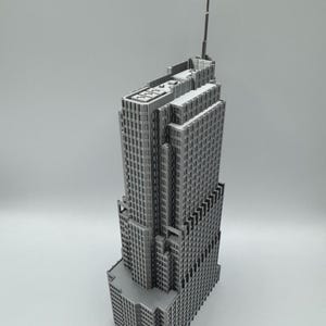 May include: A gray, detailed model of a skyscraper with multiple tiers and a tall antenna. The building has many windows and a textured facade, showcasing architectural detail. The model is set against a plain background.