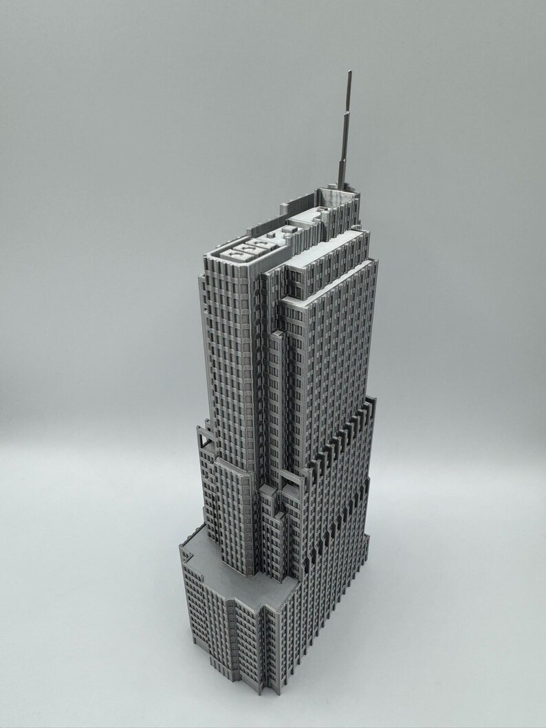 May include: A gray, detailed model of a skyscraper with multiple tiers and a tall antenna. The building has many windows and a textured facade, showcasing architectural detail. The model is set against a plain background.