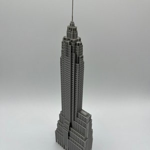 K&ouml;nnte beinhalten: Ein graues Miniaturmodell des Empire State Building. Das Modell hat ein detailliertes Design, einschlie&szlig;lich der Antenne und zahlreicher Fenster. Das Geb&auml;ude ist eine klassische Darstellung der ikonischen Architektur von New York City.