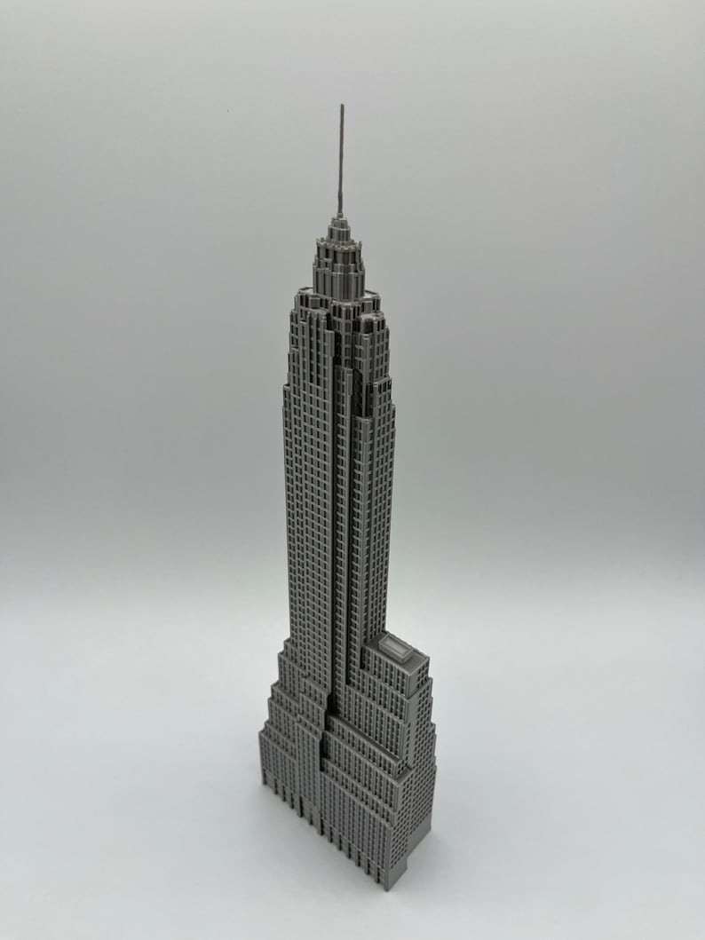 K&ouml;nnte beinhalten: Ein graues Miniaturmodell des Empire State Building. Das Modell hat ein detailliertes Design, einschlie&szlig;lich der Antenne und zahlreicher Fenster. Das Geb&auml;ude ist eine klassische Darstellung der ikonischen Architektur von New York City.