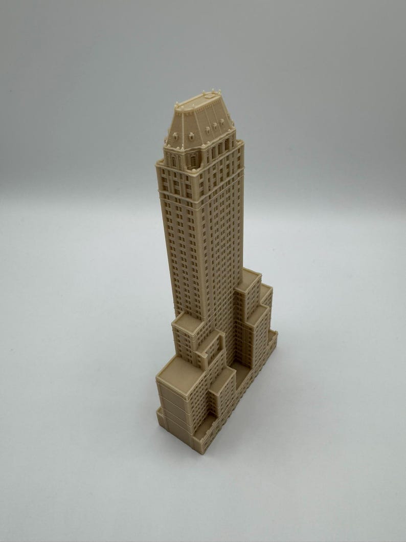 Może przedstawiać: Beżowy miniaturowy model wieżowca z szczeg&oacute;łowymi elementami architektonicznymi. Model ma wysoką, prostokątną konstrukcję gł&oacute;wną z wieloma oknami i szczeg&oacute;łowym dachem. Podstawa budynku ma kilka mniejszych prostokątnych sekcji.