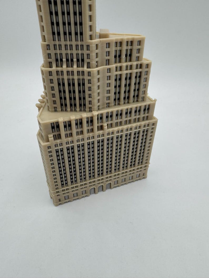 Op de afbeelding: Een beige 3D-geprint model van een hoge wolkenkrabber met veel ramen en een gedetailleerde gevel.