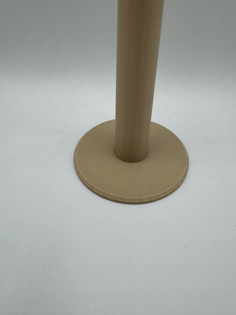 Op de afbeelding: Een beige, cilindrische standaard met een cirkelvormige basis. De standaard heeft een gladde, matte afwerking en staat tegen een witte achtergrond. De basis is een iets donkerdere tint beige dan de verticale steun.