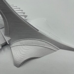 May include: White 3D printed model of a building with a curved, pointed roof and a series of steps leading up to the roof.