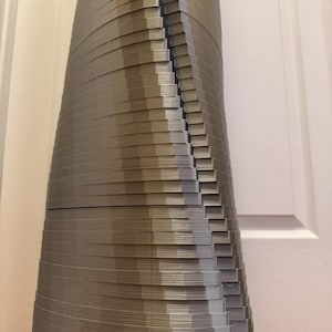 May include: A 3D printed sculpture made of stacked layers of plastic, creating a unique and abstract design. The sculpture is a light grey colour and has a smooth, slightly textured surface.