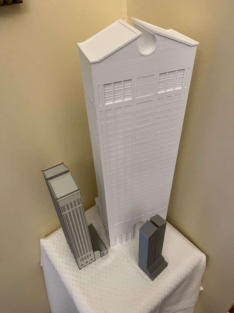 May include: Three white 3D printed model buildings. The tallest building is white and has a rounded roof. The two smaller buildings are gray and have flat roofs.