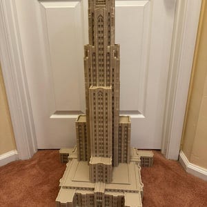 Puede incluir: Un modelo impreso en 3D detallado de un edificio alto de color beige con un techo puntiagudo y muchas ventanas. El modelo est&aacute; sobre una alfombra marr&oacute;n.