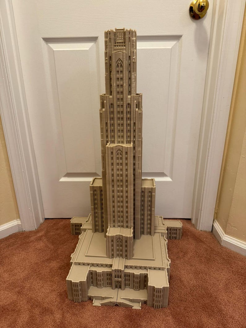 Puede incluir: Un modelo impreso en 3D detallado de un edificio alto de color beige con un techo puntiagudo y muchas ventanas. El modelo est&aacute; sobre una alfombra marr&oacute;n.