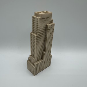 May include: A beige-colored miniature skyscraper model with a detailed facade. The building has a stepped design and a tall, rectangular tower. The model is a representation of a famous building.