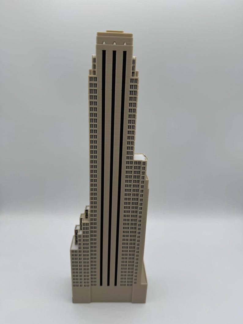 May include: A beige skyscraper model with black vertical stripes and numerous rectangular windows. The building has a stepped design and a flat roof. The model is a miniature representation of a famous building.