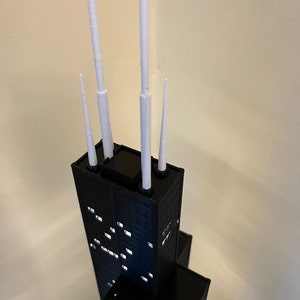 May include: A black and white model of a skyscraper with four white spires on top.