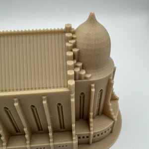 May include: A beige 3D-printed model of a cathedral, showcasing architectural details. The model features a domed structure, arched windows, and a detailed roofline. The overall design is a miniature representation of a religious building.