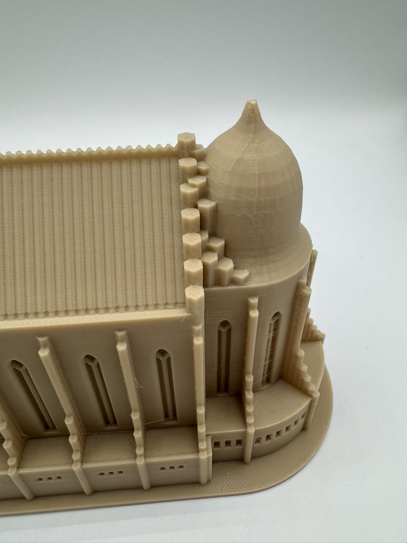May include: A beige 3D-printed model of a cathedral, showcasing architectural details. The model features a domed structure, arched windows, and a detailed roofline. The overall design is a miniature representation of a religious building.